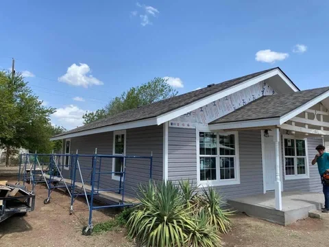 Gray siding and white window trim with scaffolding alongside the same home.
