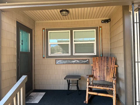 A sheltered porch nook with window trim and a wooden chair at Bruce’s home.