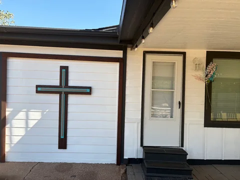 White horizontal siding, dark door trim and a decorative cross at Bruce’s home.