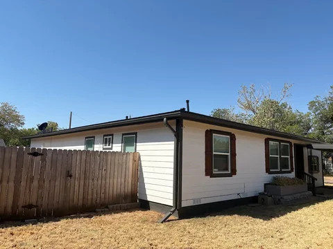 Bruce’s own home with white Hardie siding, darker window trim and shutters, and a black roof.